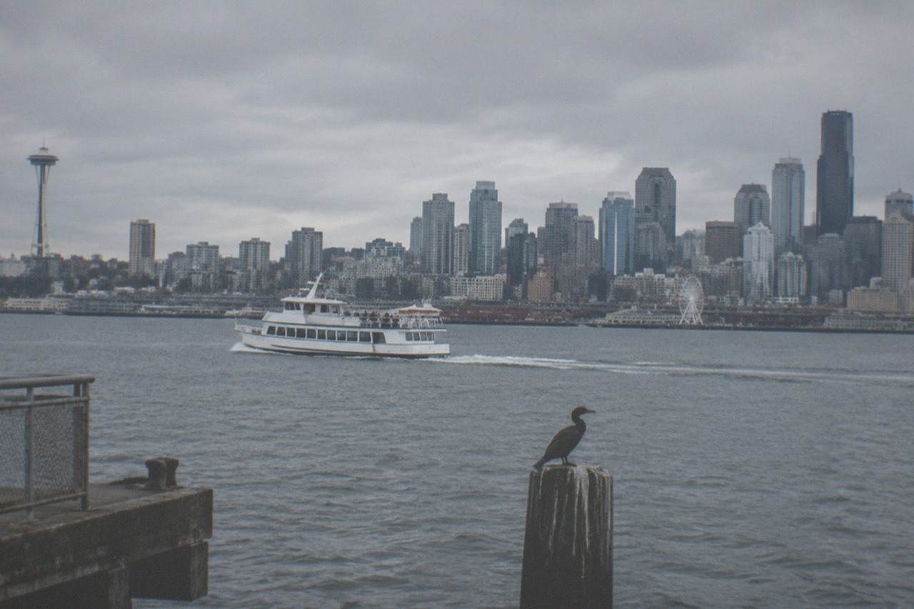 A tour boat crossing Elliott Bay with the Seattle skyline behind it under an overcast sky