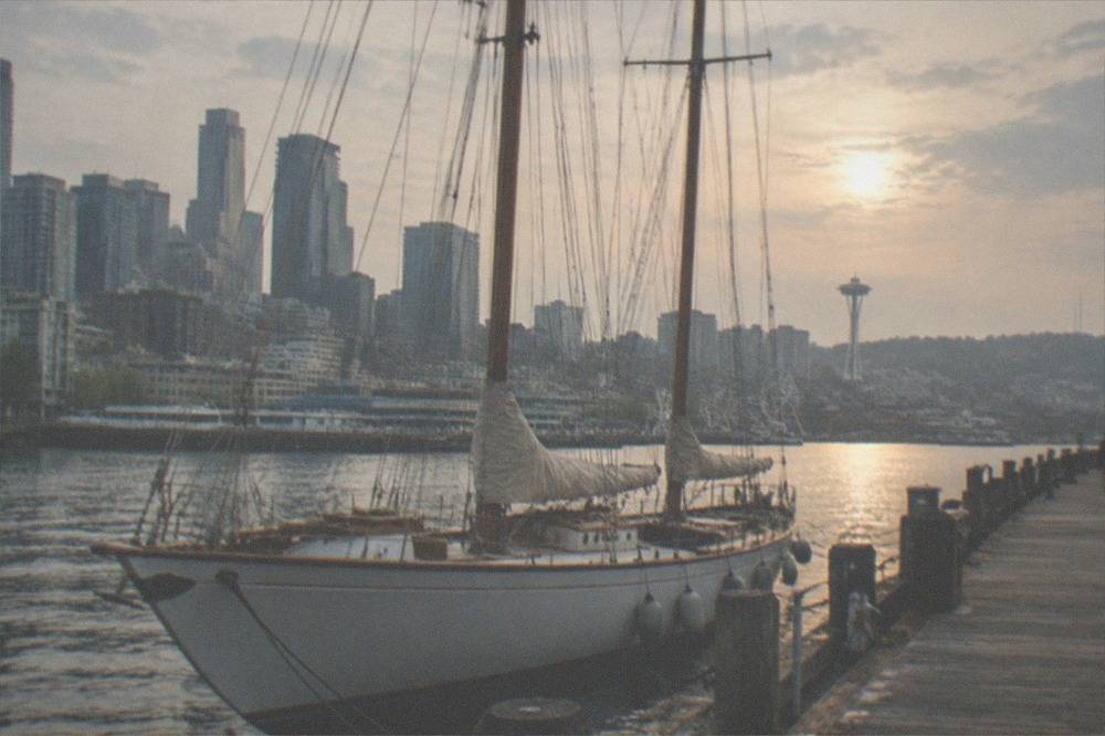 A classic 70-foot sailing boat moored at a Seattle pier with downtown buildings behind