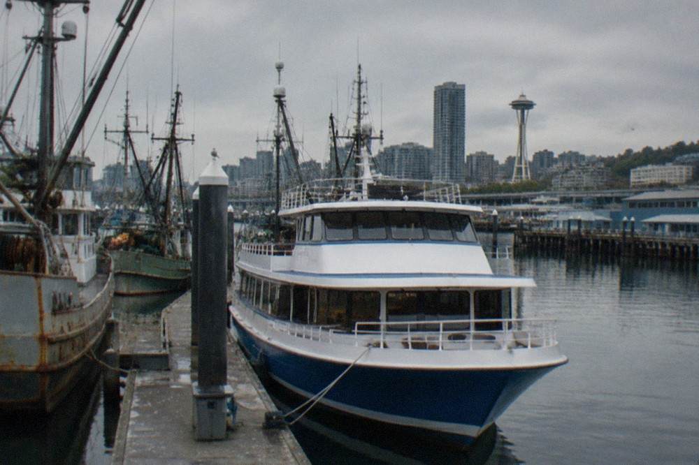 A dinner cruise boat tied up at a dock at Fishermen's Terminal, with masts of fishing boats and a gray Seattle sky behind it