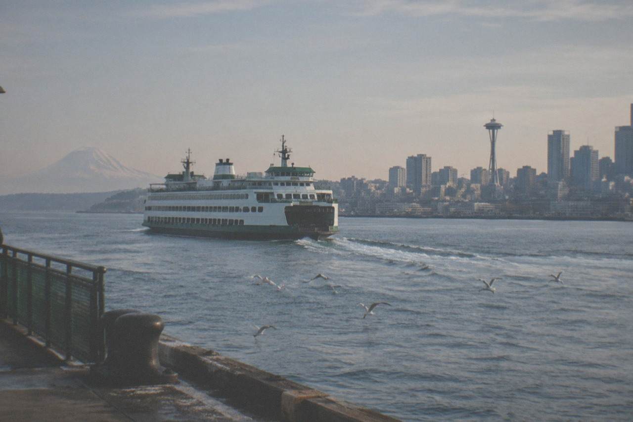 A Washington State ferry crossing Puget Sound with the Seattle skyline and Mount Rainier behind it