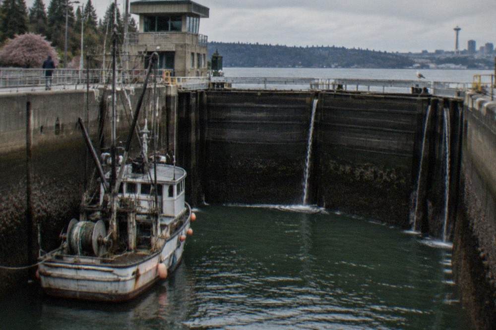 A fishing boat tied inside a ship canal lock chamber while water drains around it