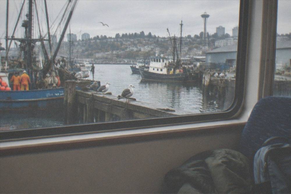 A folded jacket and small daypack on the seat of a tour boat with Seattle piers visible through a window