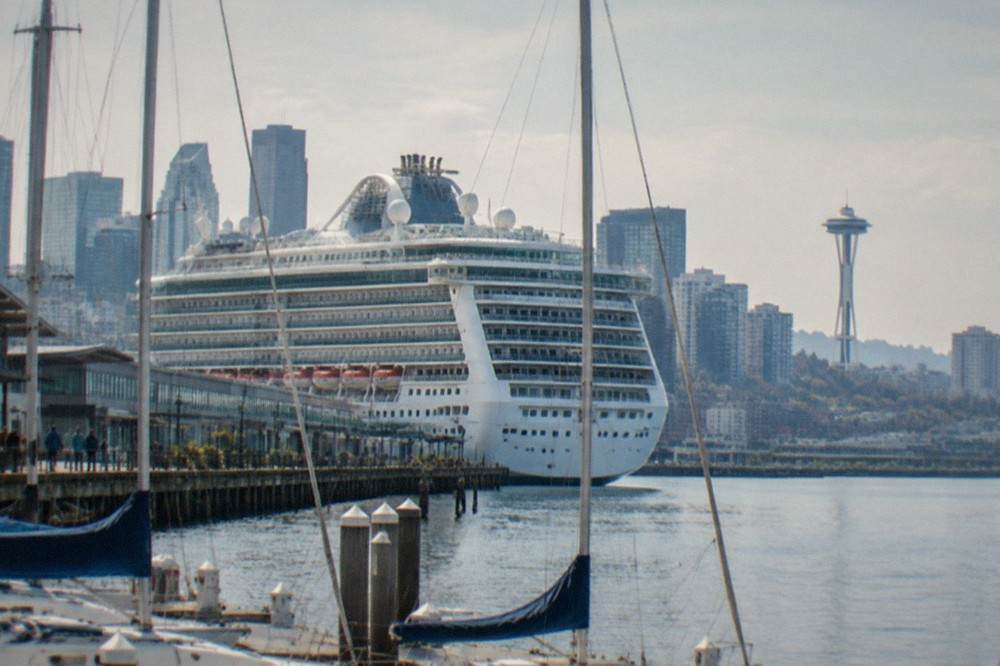 A large cruise ship moored at a Seattle terminal with masts and downtown buildings in the background.