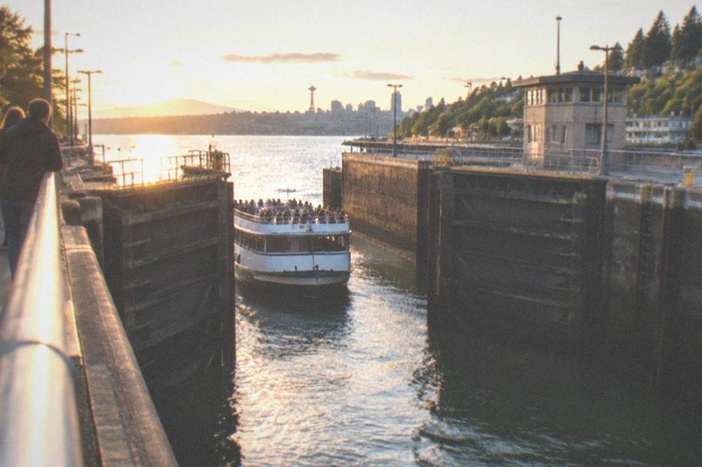A tour boat passing through a canal lock gate with visitors watching from the side.