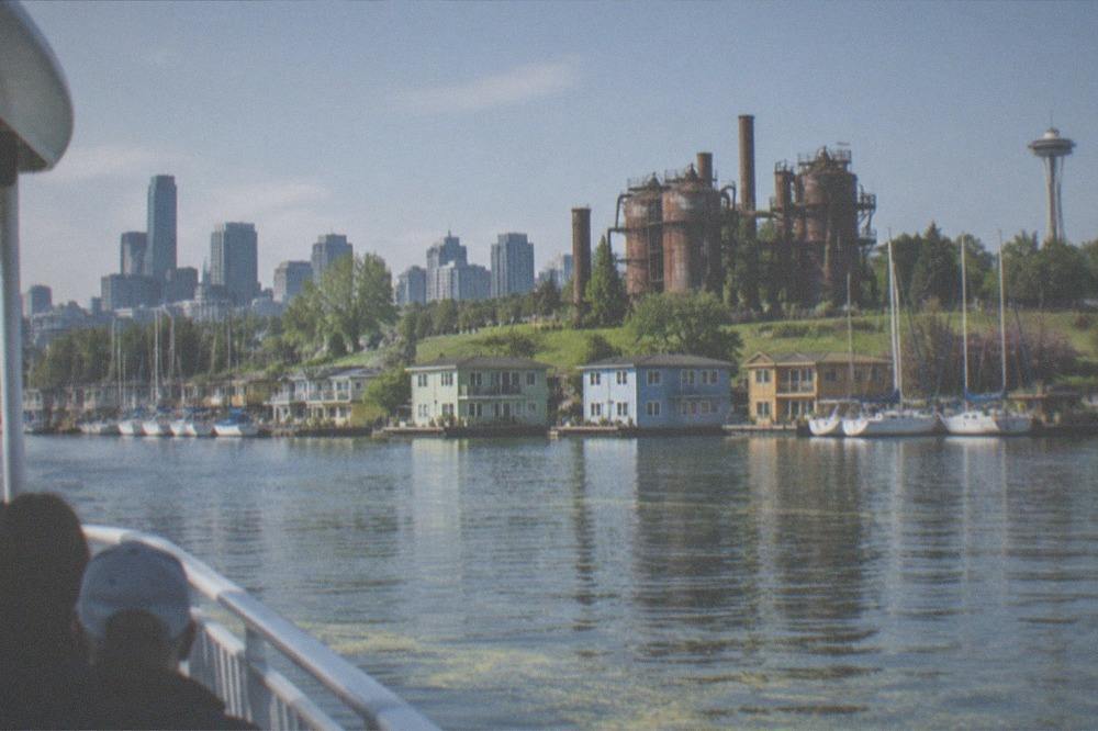 A small cruise boat passing floating homes on Lake Union under a bright sky