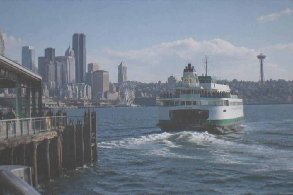 Green and white ferry vessel departing a downtown terminal with passengers on deck