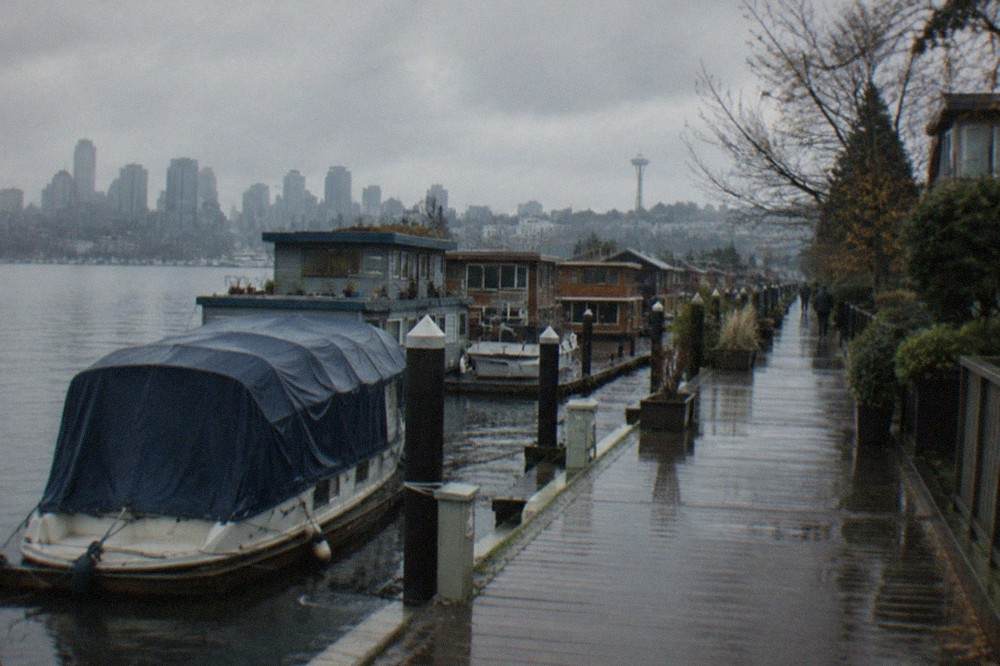 A covered charter boat tied up at a Lake Union dock with houseboats along the shoreline