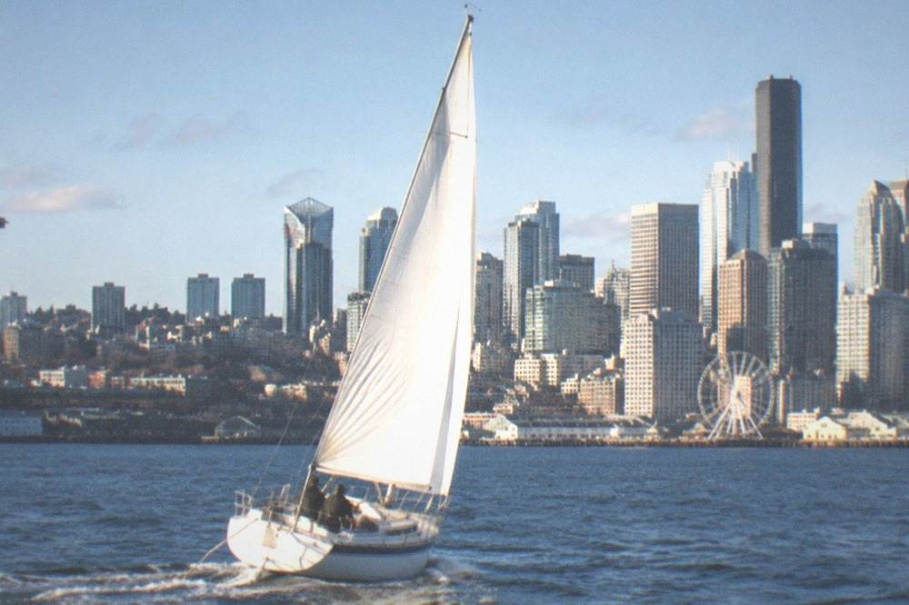 A sailing cruise boat heeling slightly on Elliott Bay with downtown towers behind