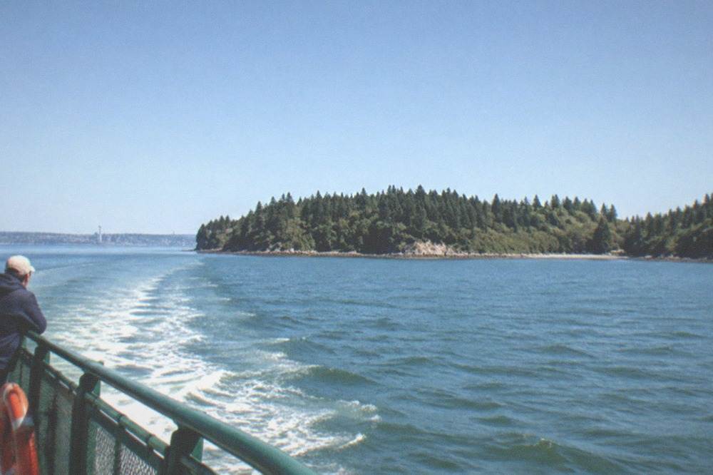 Open water of Puget Sound under a wide sky with forested islands on the horizon